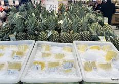 Whole pineapples sit behind containers of peeled and cored pineapples on ice.