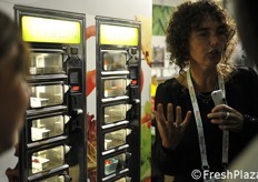 Fresh produce vending machine offering fruits and vegetables in small trays.