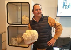 DeMartino standing next to a typical small farm which would be set up in a store or restaurant. He is holding a block that is growing a Lion's Mane mushroom. DeMartino says the Lion's Mane is gaining in popularity and has many different uses.